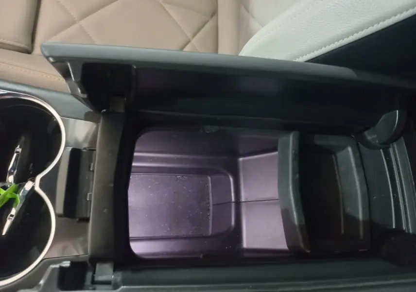 Vue rapprochée de la console centrale ouverte du DS7 Crossback, montrant le rangement intérieur noir et les sièges cuir beige.