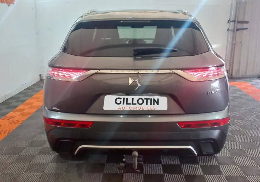 Vue arrière d'un DS7 Crossback gris foncé avec feux LED allumés et attelage visible en intérieur showroom.