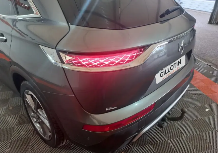 Vue 3/4 arrière droite du DS7 Crossback gris foncé avec feux arrière allumés et attelage visible.