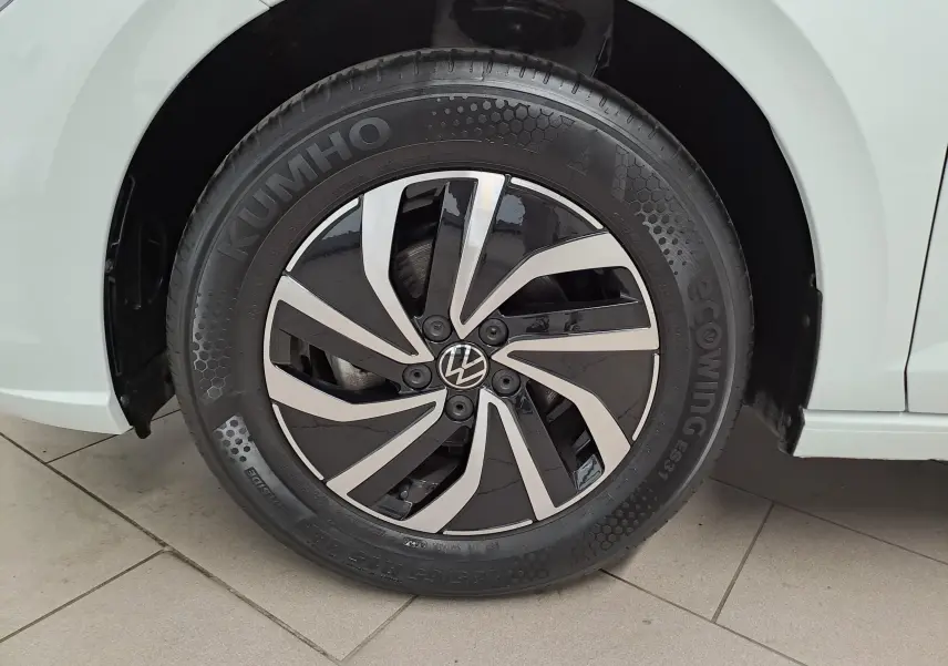 Gros plan sur la roue avant gauche d'une Volkswagen Polo blanche, avec jante alliage noire et argentée au design moderne.