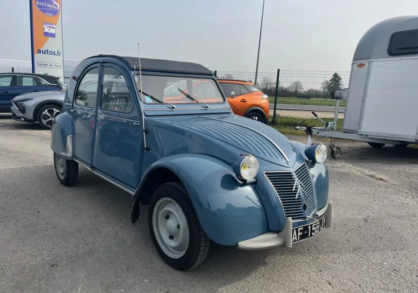 Citroën 2 CV bleu clair vue 3/4 avant droit, toit souple noir et phares ronds caractéristiques.