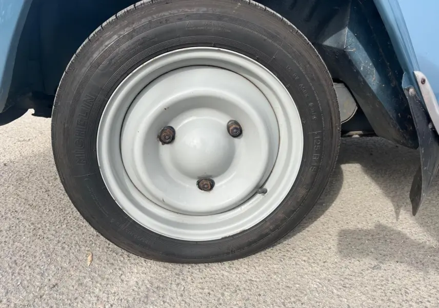 Gros plan sur la roue avant droite blanche d’une Citroën 2CV bleu clair de 1960, avec pneu Michelin visible.