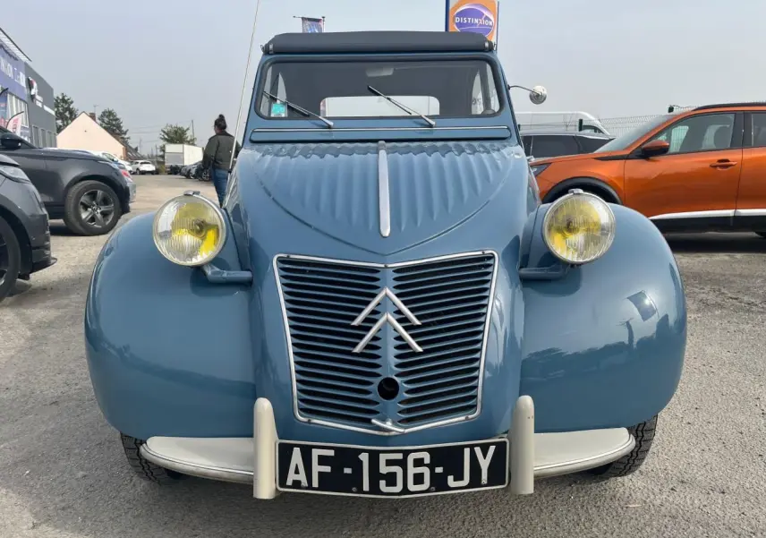 Vue de face d'une Citroën 2 CV bleu clair de 1960 avec phares jaunes caractéristiques et calandre en métal chromé.