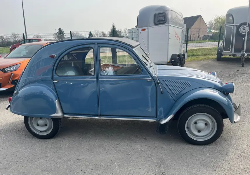 Profil côté gauche d'une Citroën 2CV bleu clair de 1960 avec toit ouvrant en toile partiellement replié.