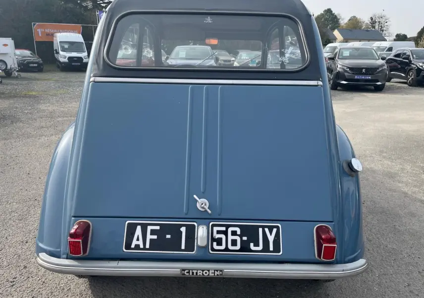 Vue arrière d'une Citroën 2CV bleu clair de 1960, avec ses feux rouges caractéristiques et plaque d'immatriculation noire.