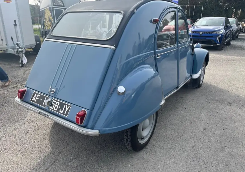 Vue 3/4 arrière droite d'une Citroën 2CV bleu clair de 1960 avec toit souple noir et plaques d'immatriculation françaises.