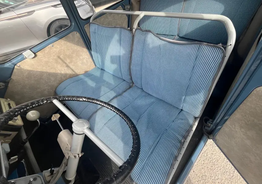 Intérieur de Citroën 2 CV 1960 bleu clair, vue plongeante sur siège avant à coussins rayés et volant fin noir.