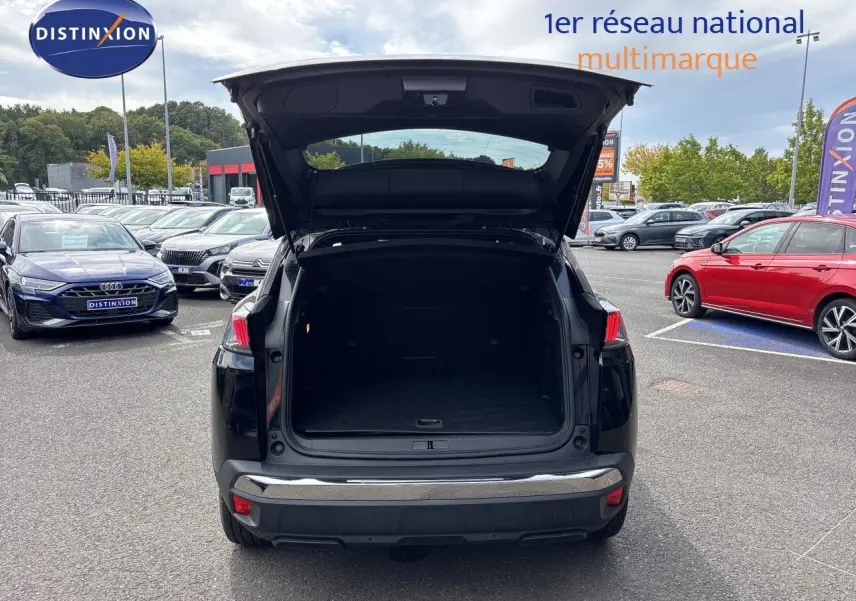 Vue arrière de la Peugeot 3008 HYBRID noire métal 2024 avec coffre ouvert sur parking multimarque.
