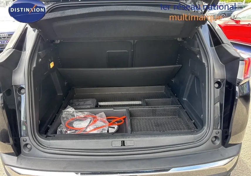 Coffre ouvert d’un Peugeot 3008 HYBRID noir métal, vue arrière montrant l’espace de rangement et câbles de recharge.
