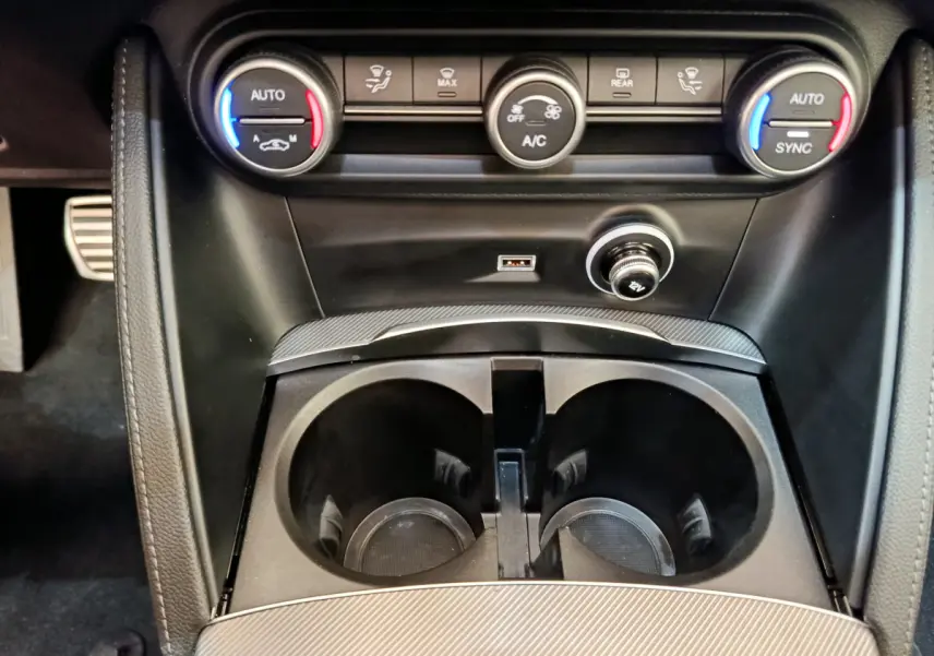 Gros plan sur la console centrale de l'Alfa Romeo Stelvio 2024 gris foncé, avec commandes climatisation et prises USB visibles.