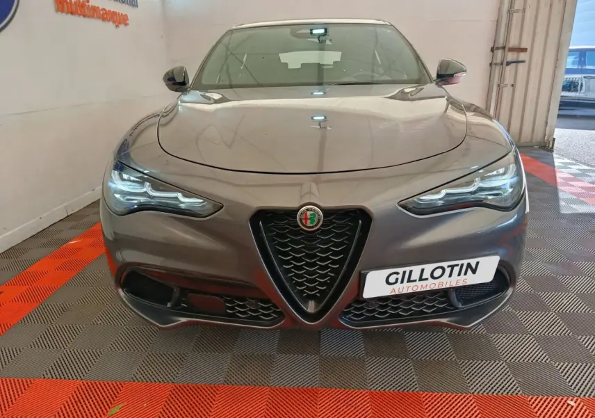 Vue frontale d'un Alfa Romeo Stelvio gris foncé avec calandre triangulaire distinctive et phares LED allumés.