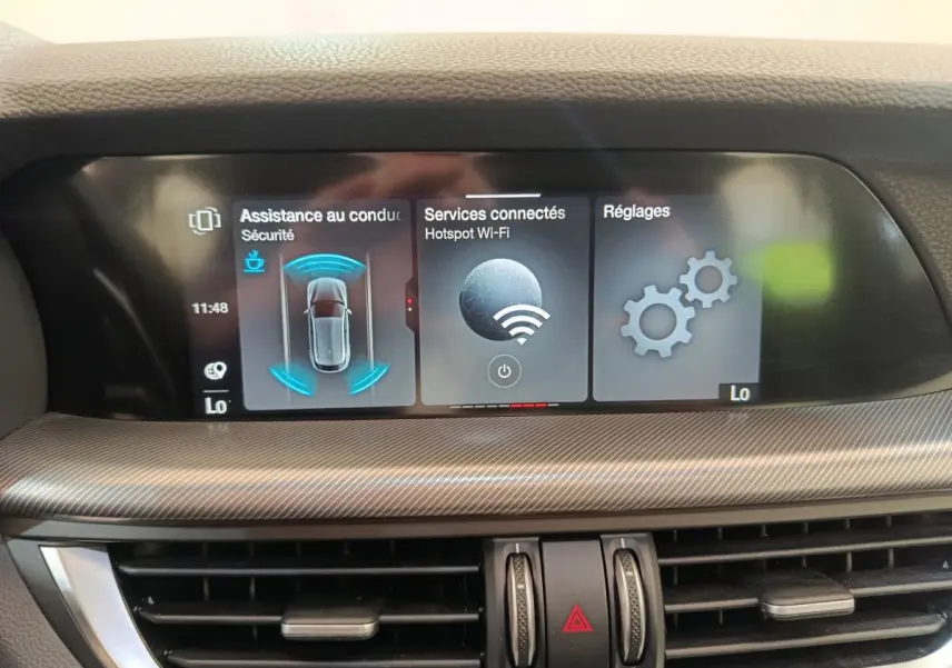 Écran tactile central de l'Alfa Romeo Stelvio 2024 affichant l'assistance conduite, Wi-Fi et réglages, intérieur gris.