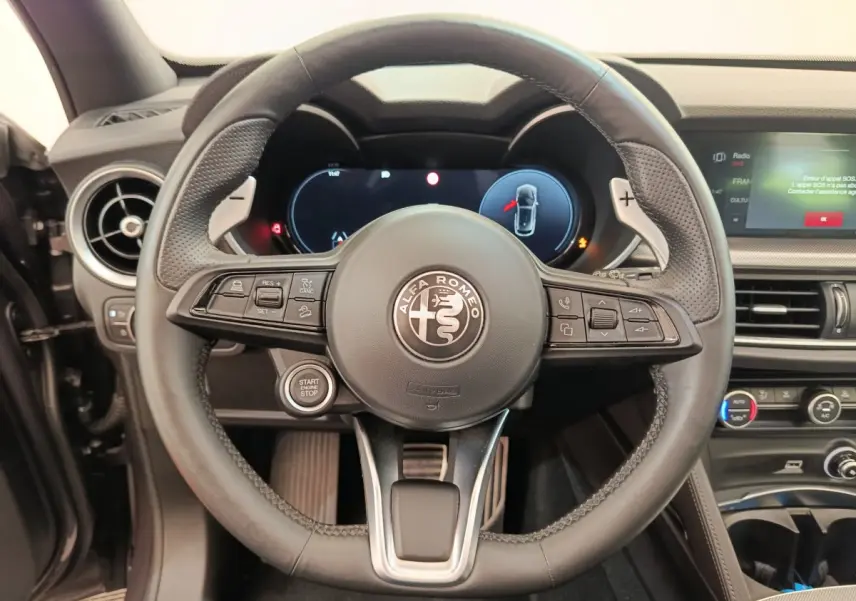 Vue rapprochée du volant cuir noir d'Alfa Romeo Stelvio 2024 avec tableau de bord numérique et bouton start/stop.