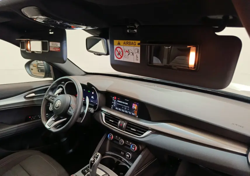 Vue intérieure côté conducteur de l'Alfa Romeo Stelvio gris foncé 2024, avec tableau de bord et écran tactile allumés.