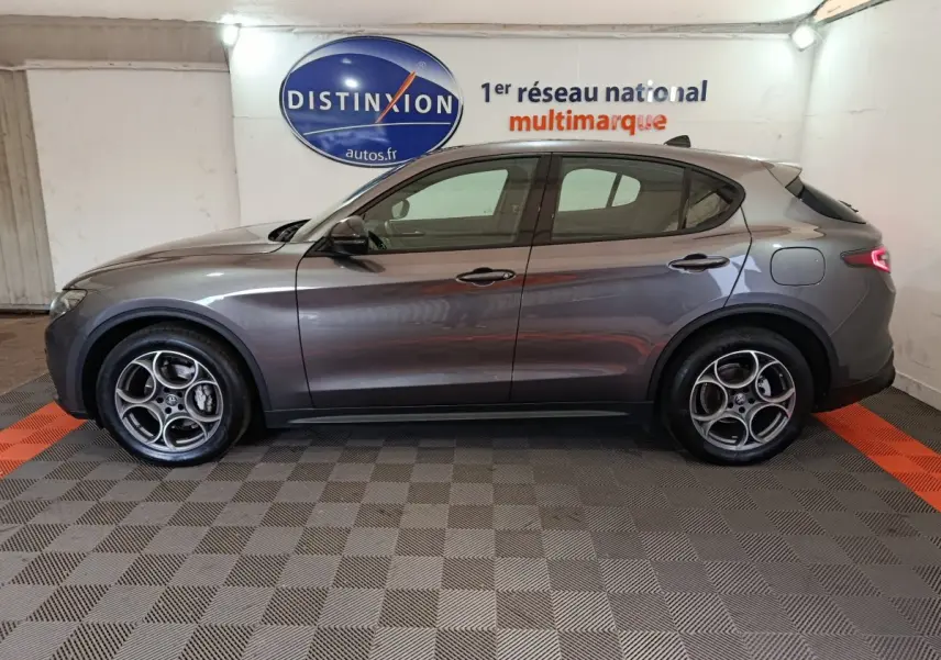 Vue de profil côté gauche d'un Alfa Romeo Stelvio gris foncé 2024 avec jantes distinctives à cinq cercles.