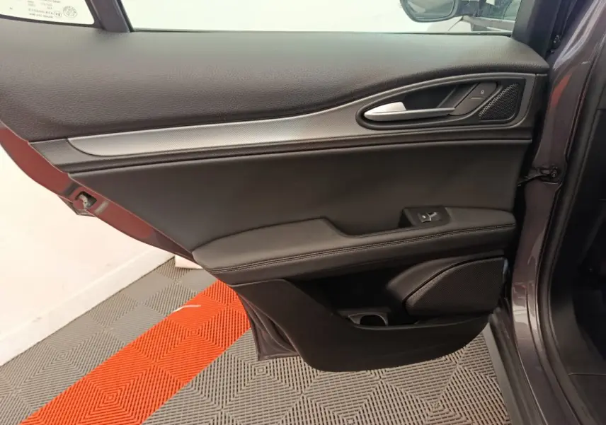 Vue côté gauche de la porte intérieure gris foncé de l'Alfa Romeo Stelvio 2024 avec poignée alu et haut-parleur intégré.