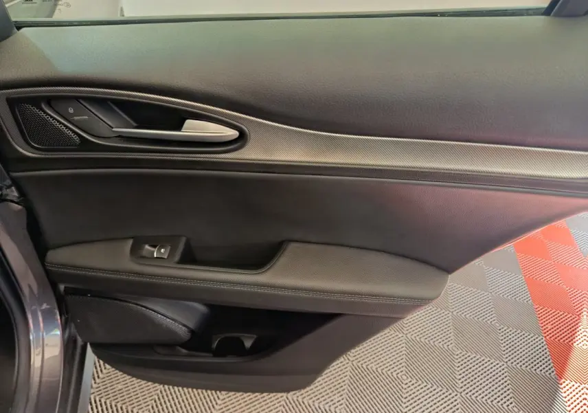 Vue rapprochée de la porte avant gauche de l'Alfa Romeo Stelvio gris foncé, avec poignée argentée et garniture noire.