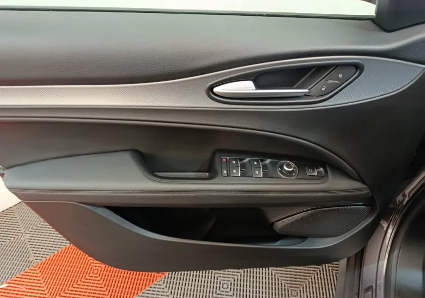 Vue latérale du panneau de porte avant gauche gris foncé d'une Alfa Romeo Stelvio 2024 avec commandes électriques et poignée argentée.