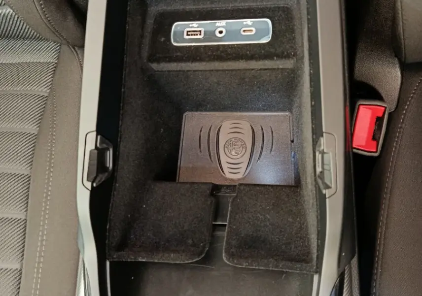 Vue plongeante sur la console centrale noire de l'Alfa Romeo Stelvio 2024 avec ports USB, AUX et zone de recharge sans fil.