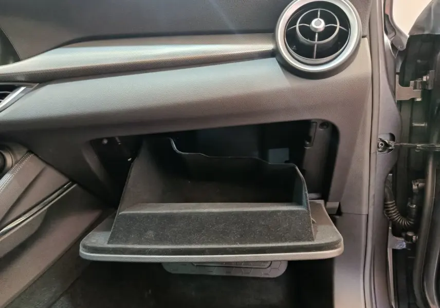 Vue intérieure côté passager de la boîte à gants ouverte de l'Alfa Romeo Stelvio gris foncé, avec aérateur rond visible.