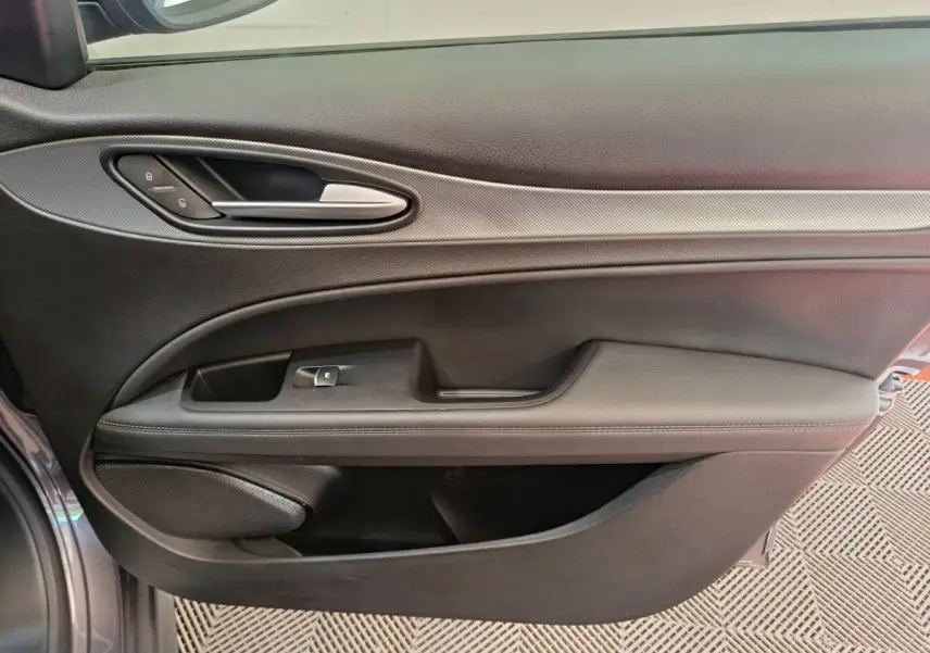 Vue intérieure côté gauche de la porte avant gris foncé de l'Alfa Romeo Stelvio avec poignée argentée et commandes de verrouillage.
