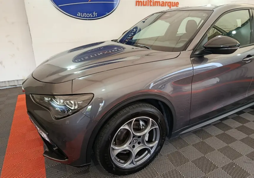 Vue 3/4 avant gauche d’un Alfa Romeo Stelvio gris foncé mettant en valeur ses phares LED et jantes alliage distinctives.
