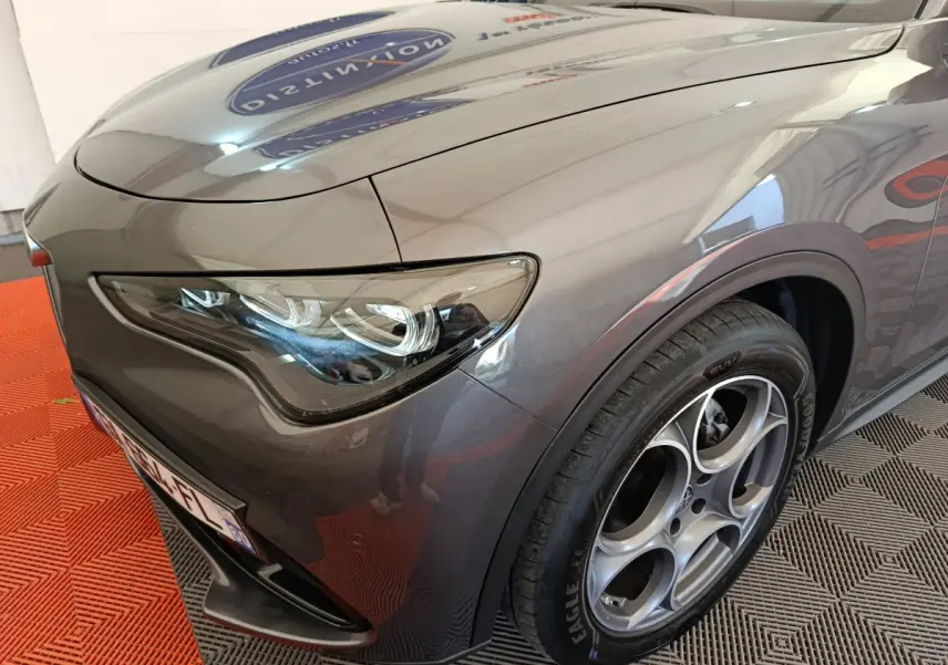 Vue 3/4 avant droit d'un Alfa Romeo Stelvio gris foncé mettant en valeur son phare LED et sa jante distinctive à cinq cercles.