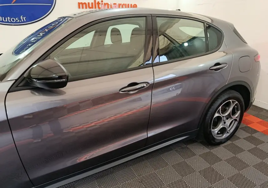 Vue latérale droite d'un Alfa Romeo Stelvio gris foncé, mettant en valeur les jantes distinctives et les lignes élégantes du SUV.