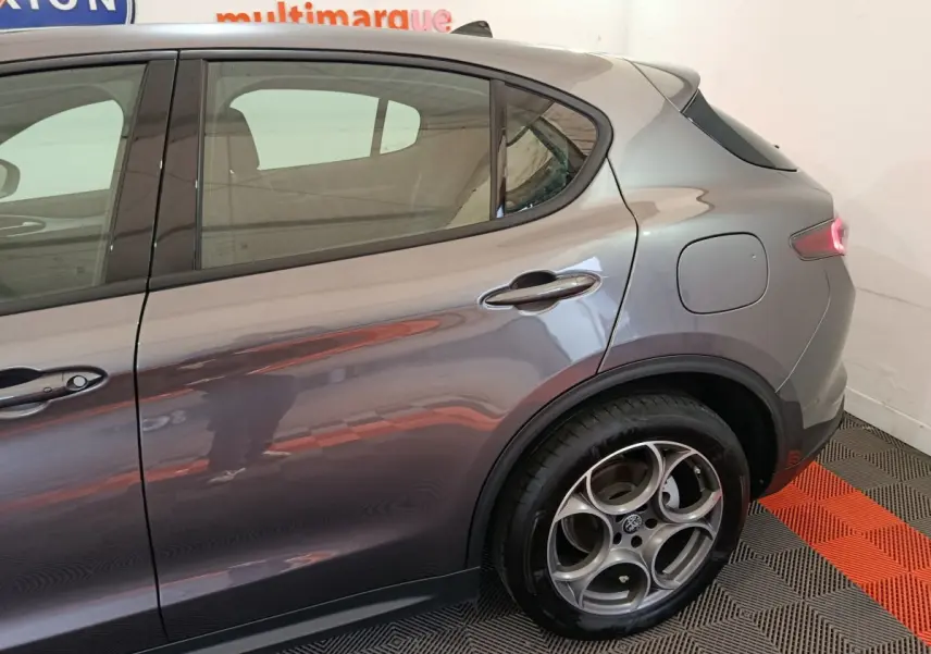 Vue latérale droite sur l'arrière d'un Alfa Romeo Stelvio gris foncé avec jante alliage distinctive et feu arrière allumé.
