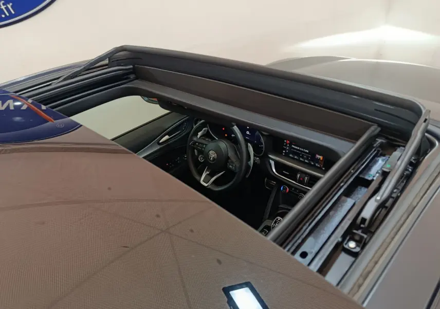 Vue plongeante sur l'intérieur noir d'un Alfa Romeo Stelvio gris foncé 2024, avec tableau de bord et volant visibles.