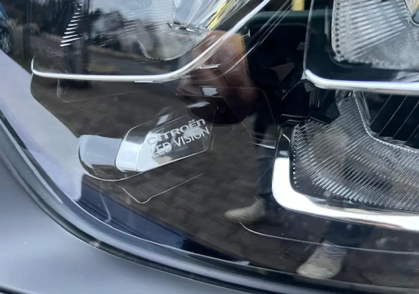 Gros plan sur le phare avant LED d'une Citroën C3 Shine noire au toit rouge, mettant en valeur l'inscription "Citroën LED Vision".