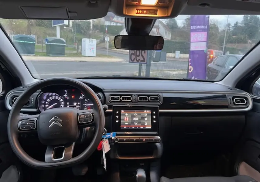Vue intérieure avant du tableau de bord noir de la Citroën C3 Shine 2023 avec volant multifonction et écran tactile central.