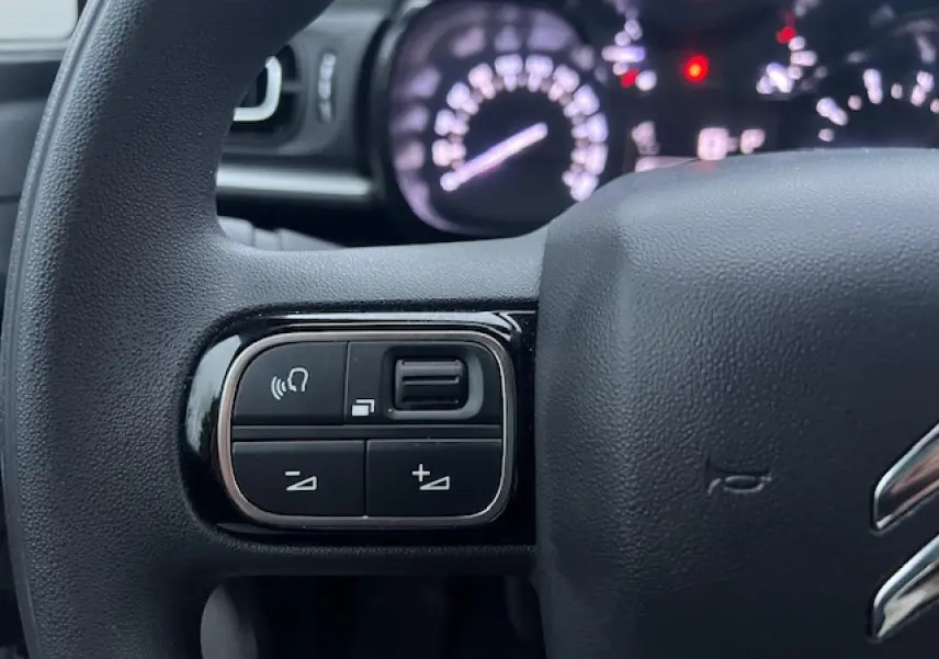Gros plan sur les commandes audio au volant d'une Citroën C3 Shine 2023, volant noir avec logo chrome partiel visible.