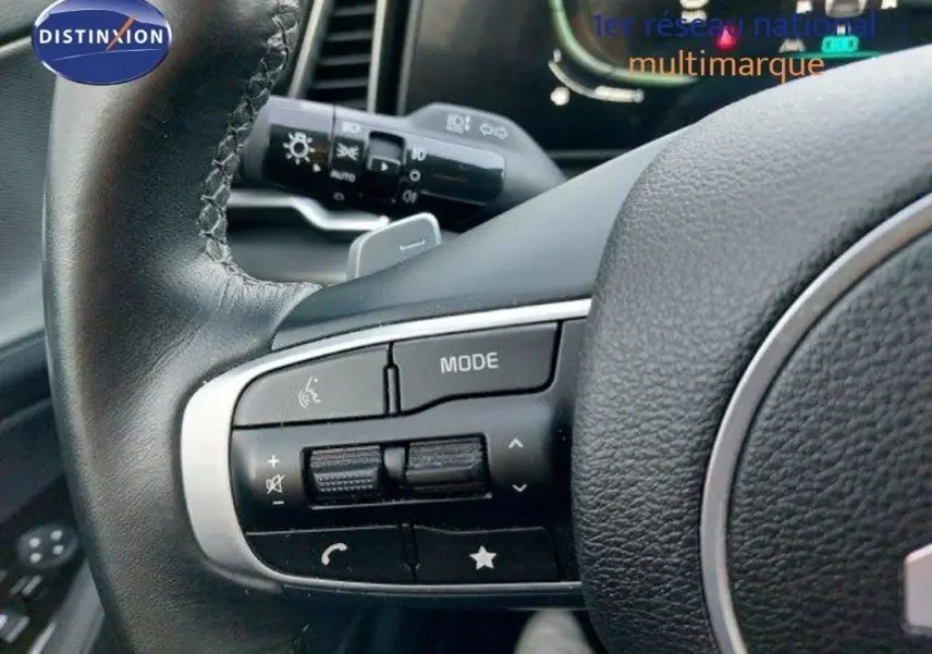 Gros plan sur les commandes au volant cuir noir du Kia Sportage 2024 hybride, avec les boutons de mode et volume visibles.