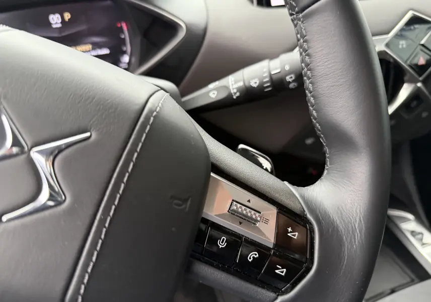 Gros plan sur le volant noir en cuir du DS3 2024, mettant en valeur les commandes intégrées et les surpiqûres blanches.