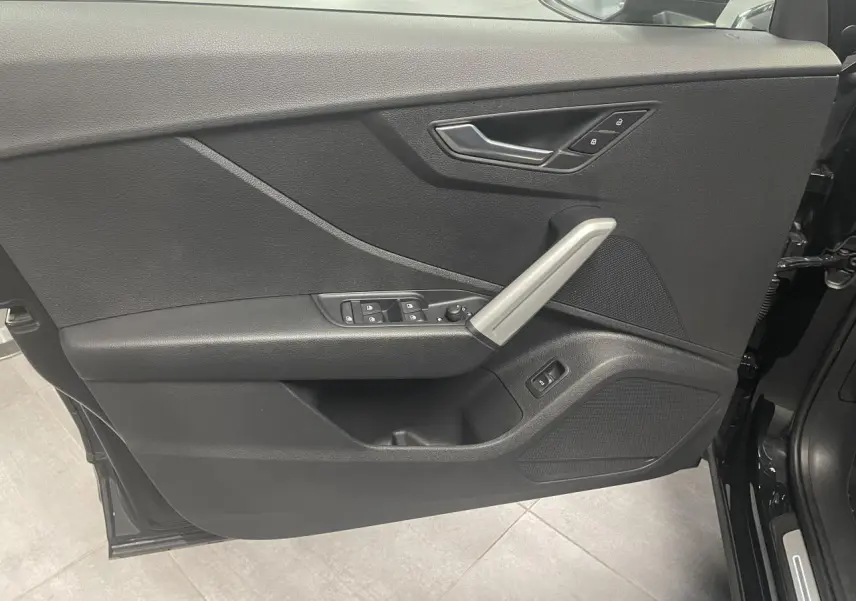 Porte avant gauche ouverte d’Audi Q2 noir métallisé 2023, avec poignée aluminium et commandes électriques.