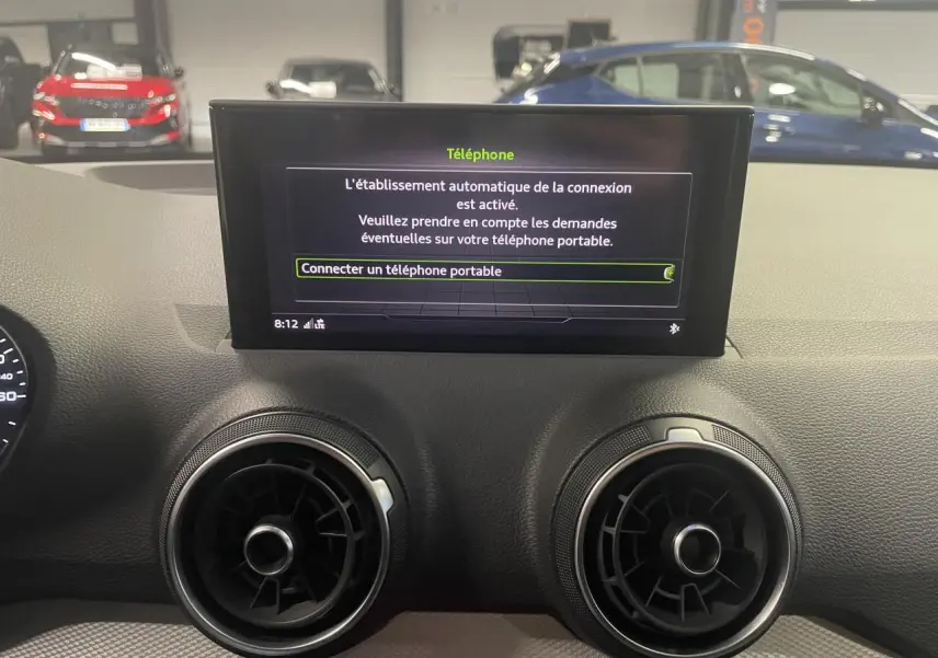 Vue intérieure du tableau de bord de l'Audi Q2 2023, écran central affichant la connexion téléphone, aérateurs ronds noirs.