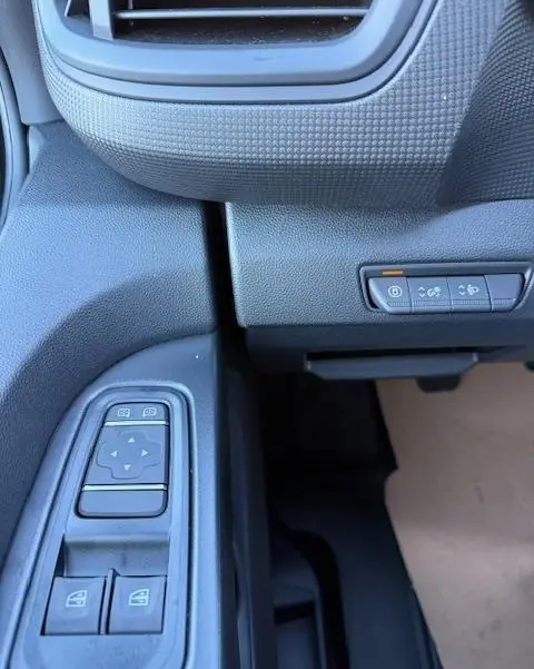 Détail des commandes de vitres électriques et boutons de fonctions sur la porte côté conducteur du Renault Trafic Fourgon gris clair 2025.