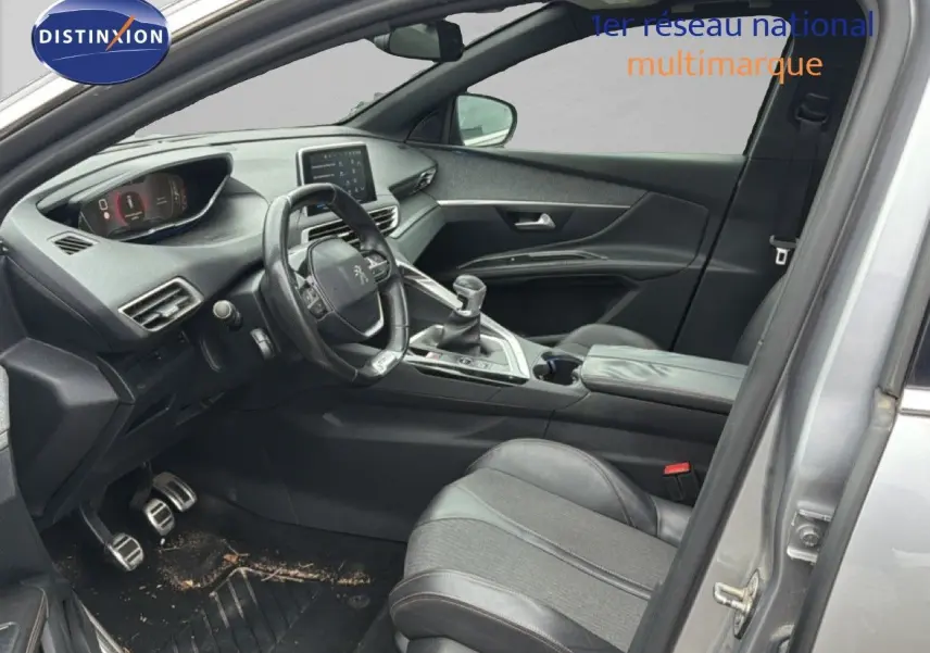 Vue intérieure côté conducteur d’un Peugeot 5008 gris Artense, avec volant compact et levier de vitesse manuel visible.