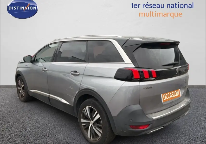 Vue 3/4 arrière droite d'un Peugeot 5008 gris Artense avec feux arrière à griffes rouges et jantes alliage bicolores.