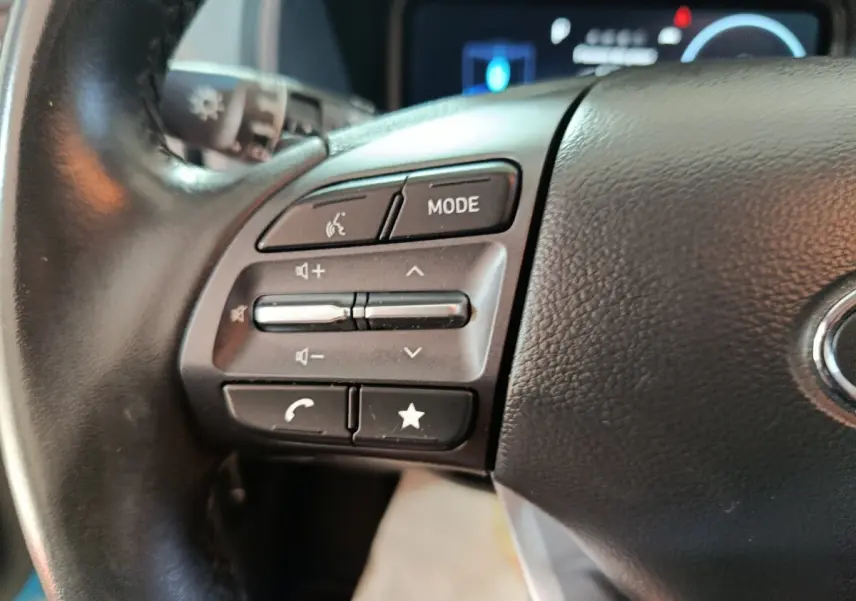 Gros plan sur les commandes du volant cuir noir du Hyundai Kona électrique 2022, côté gauche avec boutons multifonctions.