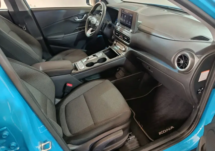 Vue intérieure côté passager du Hyundai Kona bleu 2022, avec tableau de bord central tactile et sièges tissu gris.