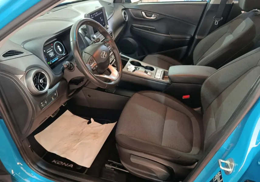 Vue intérieure côté conducteur du Hyundai Kona bleu 2022, avec tableau de bord digital et volant cuir multifonctions.