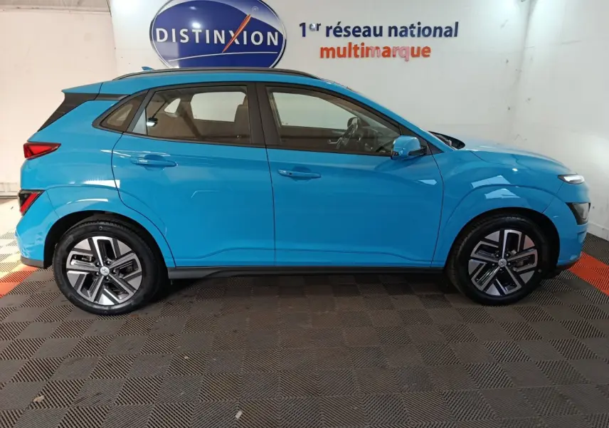 Vue de profil côté gauche d'un Hyundai Kona électrique bleu 2022 avec jantes spécifiques et toit noir contrasté.