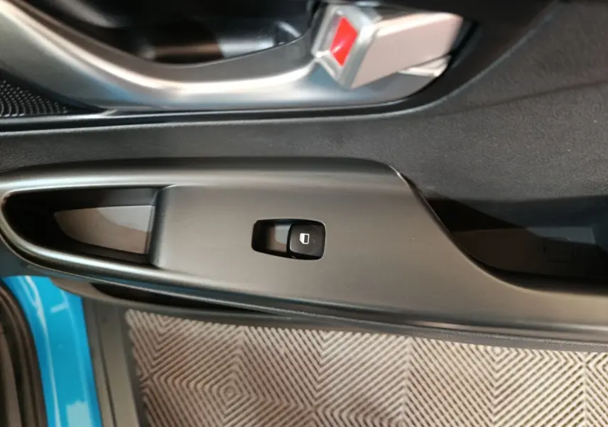 Gros plan sur le bouton de commande de la vitre électrique côté conducteur du Hyundai Kona bleu, avec poignée de porte noire.