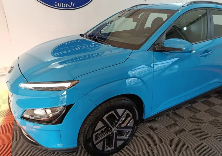Vue 3/4 avant droit d'une Hyundai Kona électrique bleu vif avec jantes spécifiques et feux LED distinctifs.