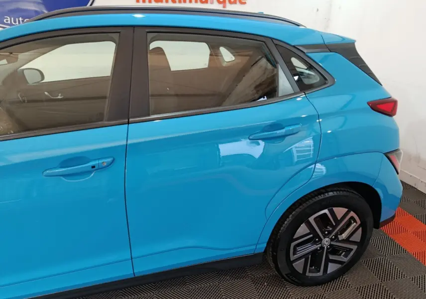 Vue latérale côté droit du Hyundai Kona électrique bleu, mettant en valeur les portes arrière et la roue arrière.