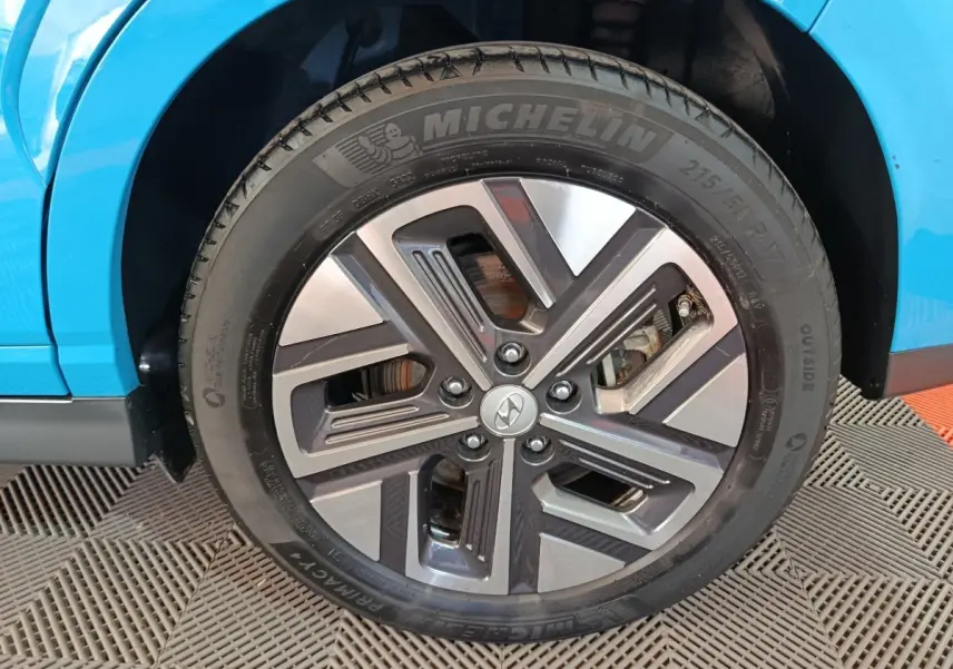 Gros plan sur la roue avant gauche d’une Hyundai Kona électrique bleue, avec jante alliage et pneu Michelin.