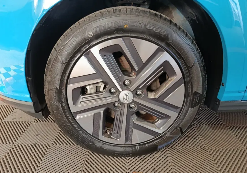 Gros plan sur la roue avant droite du Hyundai Kona électrique bleu 2022 avec jante alliage au design moderne.
