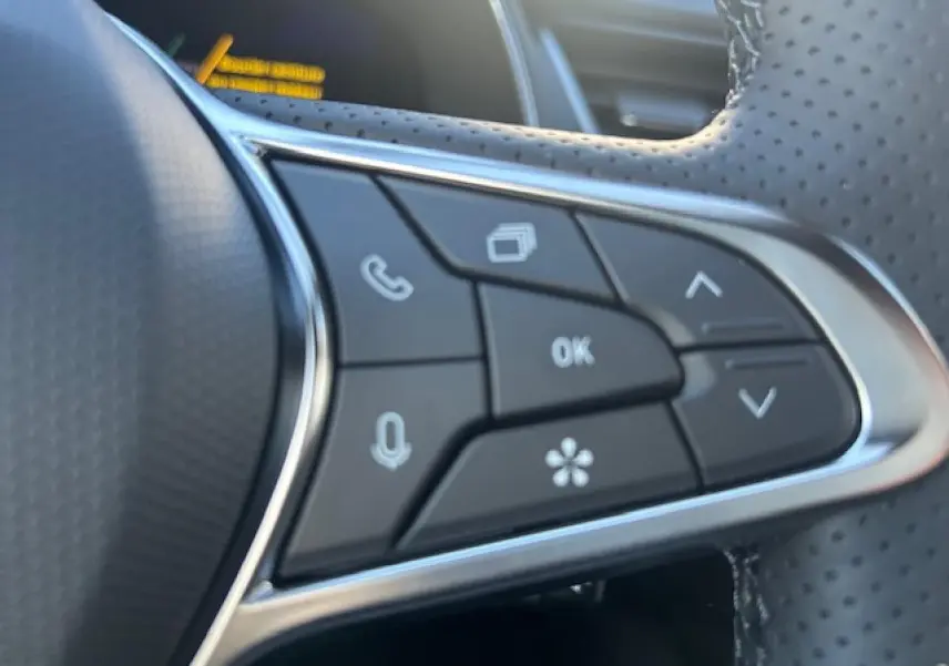 Gros plan sur les commandes multifonctions noires et argentées du volant perforé du Renault Symbioz blanc nacré.